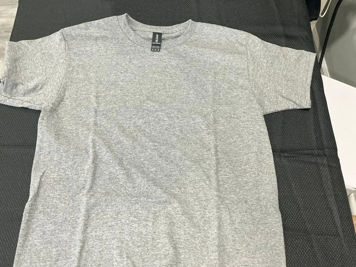 A plain sport gray Gildan youth crew-neck t-shirt laid flat and unprinted on the black pad of a heat press