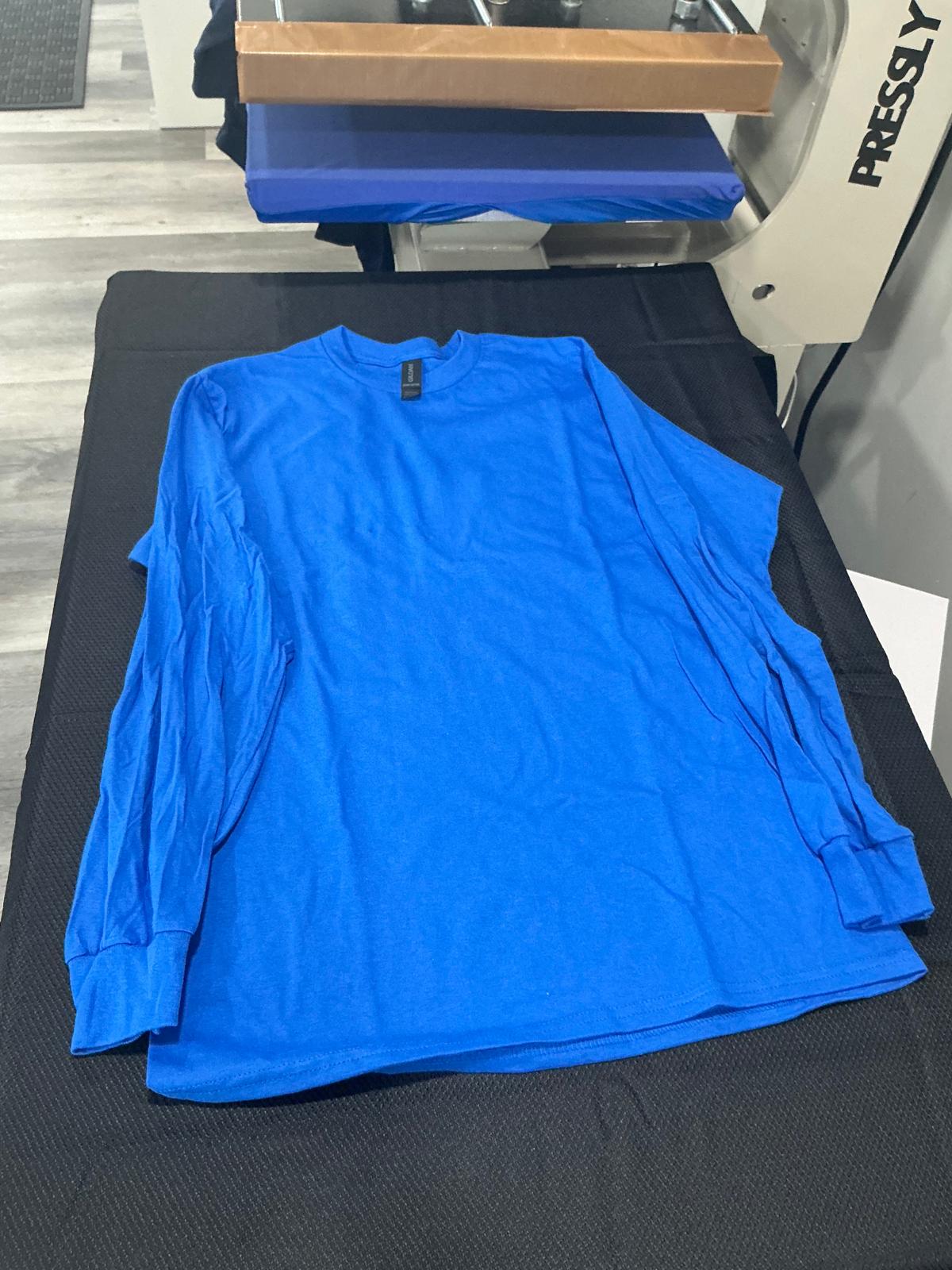 A plain royal blue long-sleeve cotton t-shirt laid flat and unprinted on the black pad of the heat press