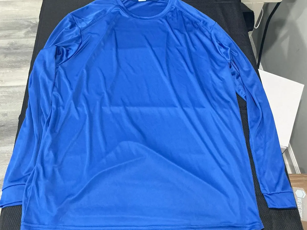 A plain royal blue long-sleeve performance t-shirt laid flat and unprinted on the black pad of a heat press