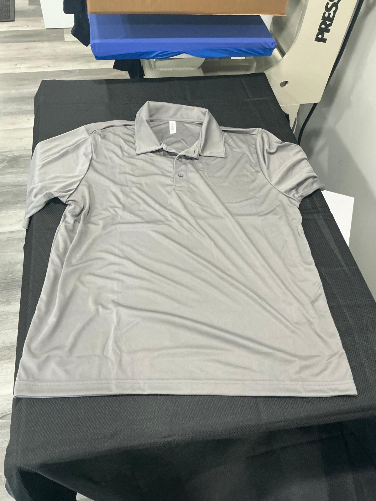 A plain gray short-sleeve polo shirt with a collar and a three-button placket, laid flat and unprinted on the black pad of the heat press